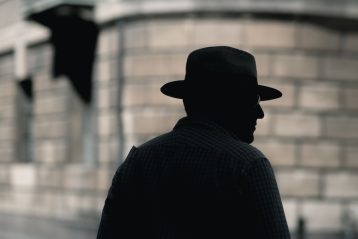 silhouette photo of a man with hat standing near concrete building at daytime