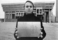 black and white photo of Carl Sagan holding a plaque in front of a brutalist architecture building