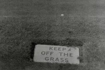 A sign reads "keep off the grass" on a lawn.