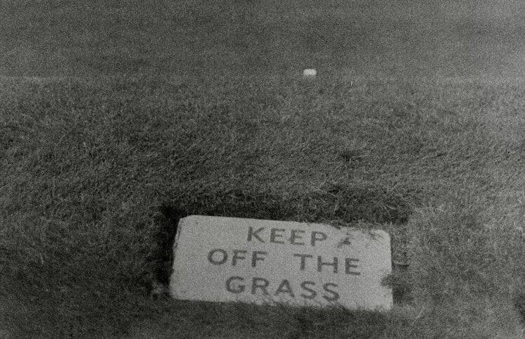 A sign reads "keep off the grass" on a lawn.
