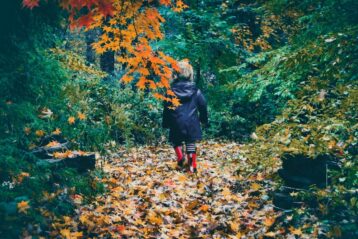 woman in black jacket and red pants walking on dried leaves on ground